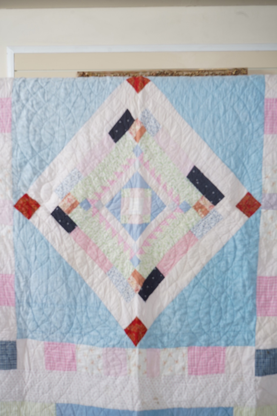 A 1900-1910 English, possibly north country hand quilted bedcover. Designed with a large central medallion, hand quilted using mostly pastel patterned and plain cottons and feature red and black cottons as highlights, ba